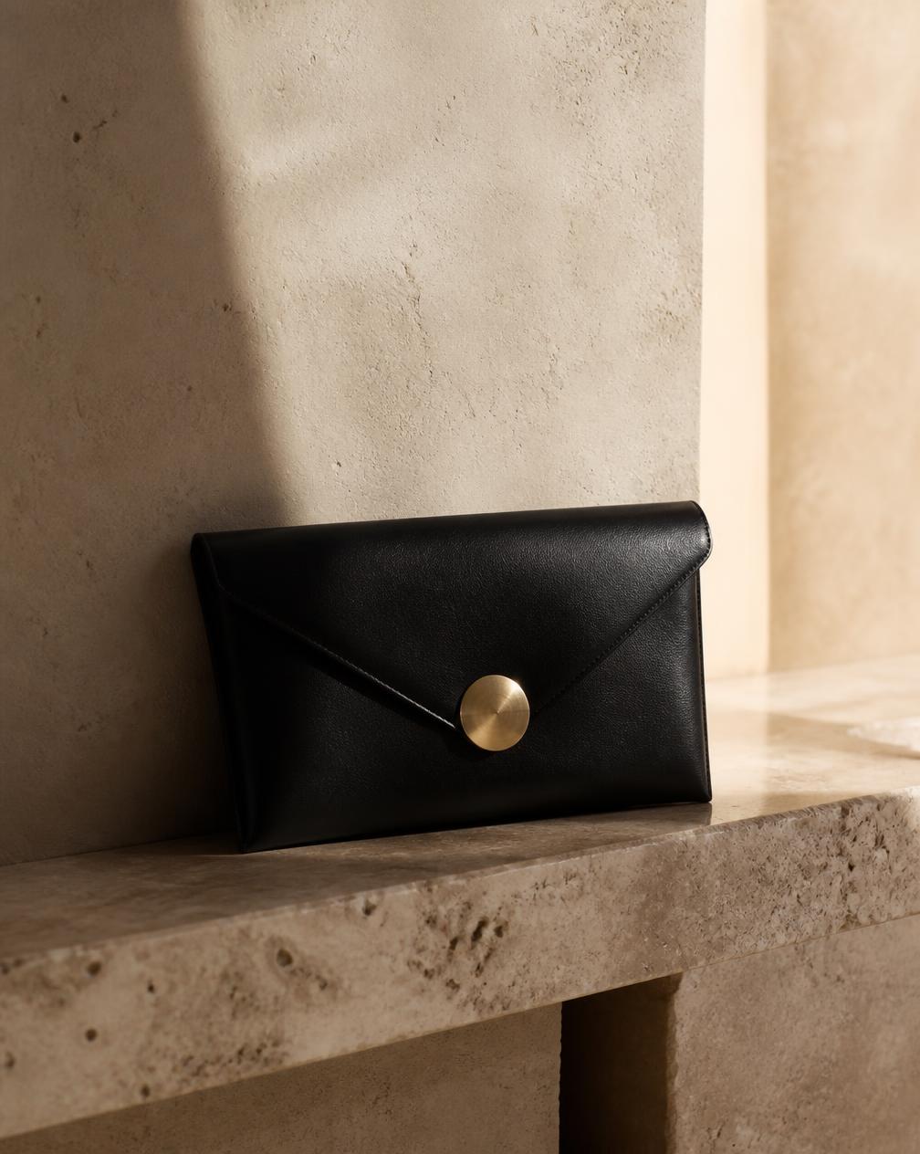 The Clutch — black leather bag on travertine, coming soon