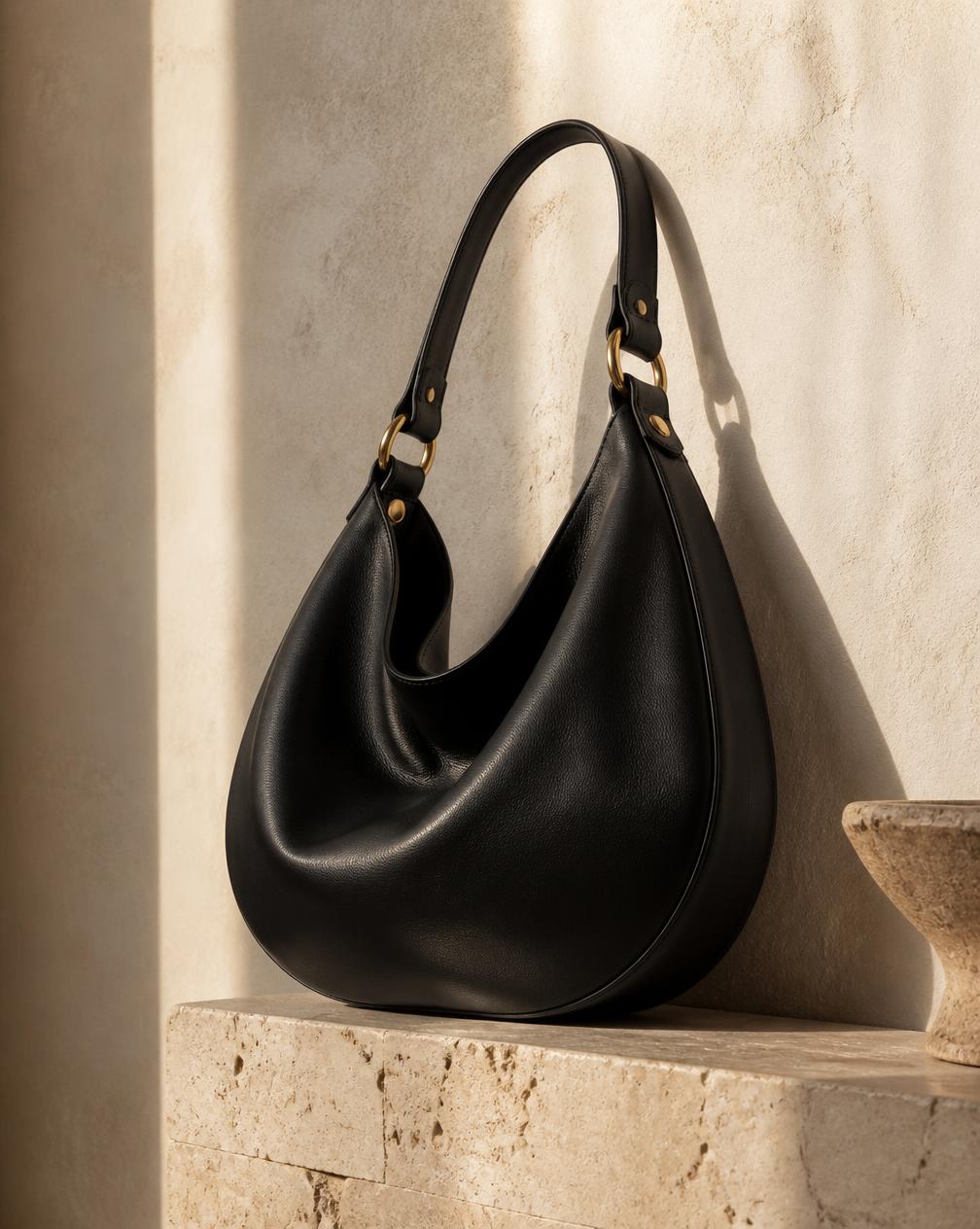 The Shoulder — black leather bag on travertine, coming soon